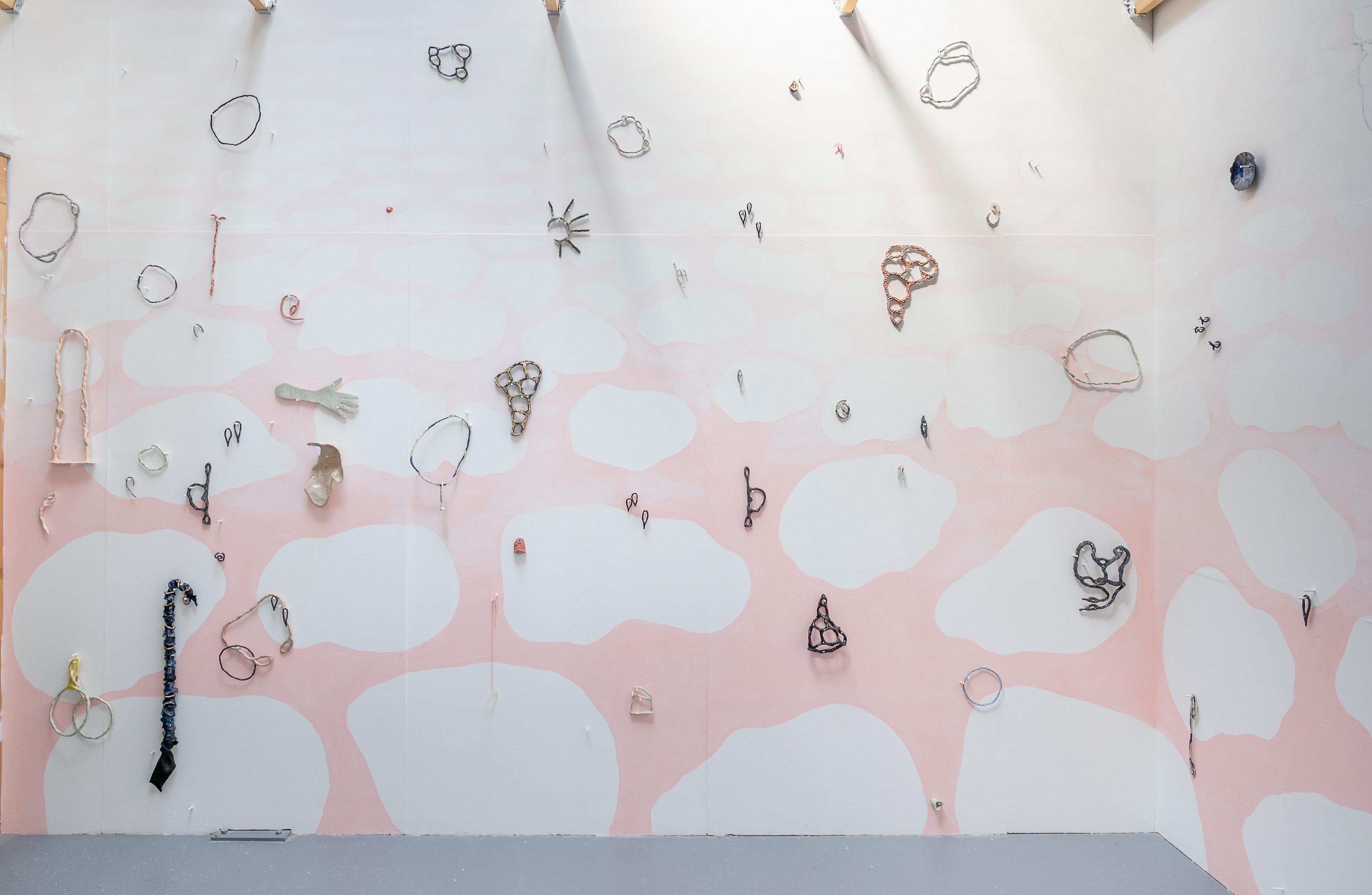 Image shows a wall with white clouds retreating over a pink sky hung with drawn sculptural shapes.